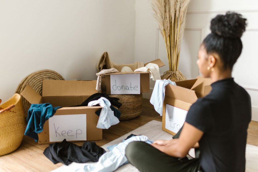 Eine Frau sortiert Kleidung in beschriftete Boxen für Spenden und Aufbewahrung.