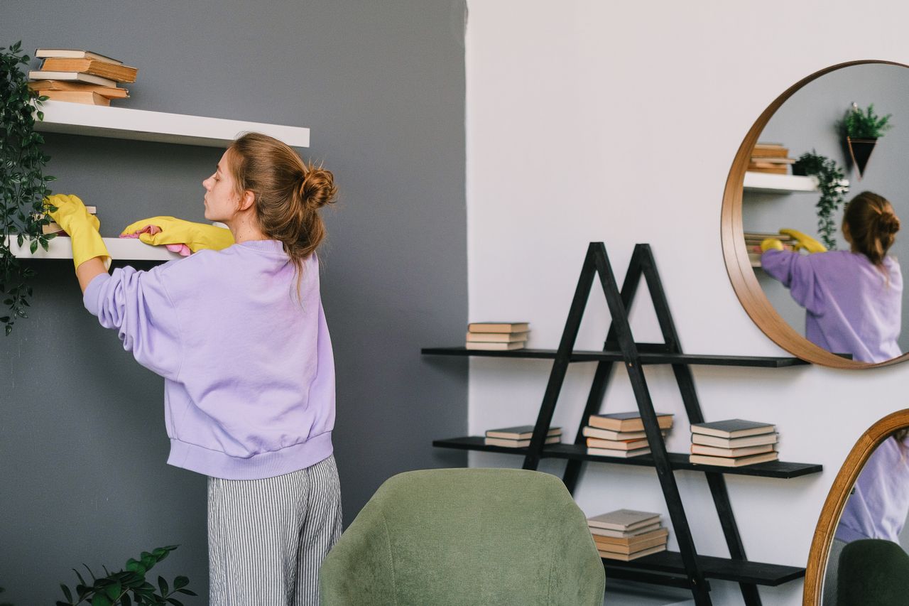 Eine Frau reinigt Regale in einem stilvollen Wohnzimmer mit Spiegeln und Dekoration.