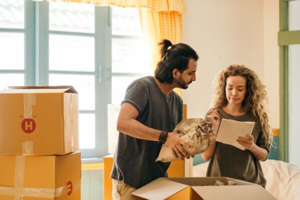 Junges Paar packt Kisten in ihrem neuen Zuhause aus und bespricht Pläne mit einer Checkliste.